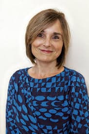 Smiling woman with short brown hair and a blue geometric patterned shirt.